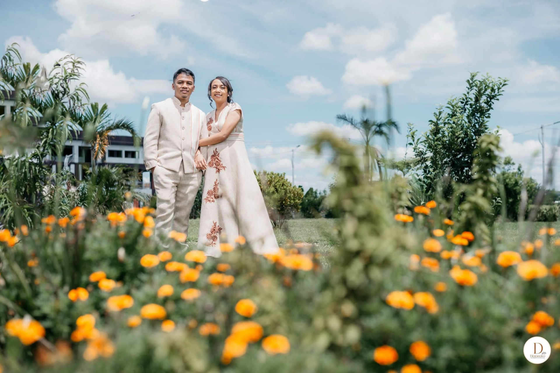 Marianne et Tojo en tenues traditionnelles dans un jardin fleuri d'orange
